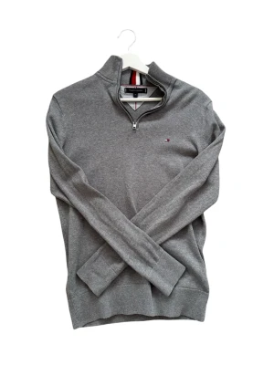 Grå halvzip tröja Tommy Hilfiger - Snygg grå tröja från Tommy Hilfiger med halv dragkedja och ståkrage. Liten logga broderad på bröstet och ribbade muddar vid ärmslut och nederkant. Passar mellan 165/175cm, pris kan diskuteras. Hör av er vid fler frågor eller funderingar 