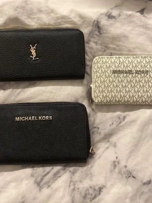  plånbok med dragkedja - Snygg svart plånbok, strukturerat läder med silverfärgad logga framtill. Plånboken har dragkedja runtom och flera fack för kort, sedlar och mynt. Insidan har klassiskt -mönster och bruna detaljer.