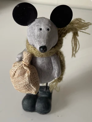 Dekorativ musfigur med halsduk - Söt musfigur i grått med stora svarta öron, grön stickad halsduk och en liten tygpåse i handen. Figuren står på svarta skor och är tillverkad i ett hårt material, troligen keramik eller liknande.En charmig musfigur klädd i en stickad halsduk och bärande en liten säck. musfigur tillverkad i sten med ben och detaljer i metall. utformad med garnhalsduk och liten tygsäck,