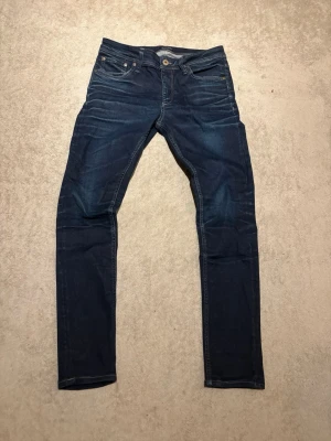 Mörkblå slim jeans med detaljer - Snygga mörkblå jeans med slim passform och klassiska fem fickor. Jeansen har kontrastsömmar och en liten läderpatch bak i midjan. Perfekta för dig som gillar en stilren och enkel look.