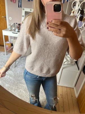 Beige stickad topp med halvärm - Mysig beige stickad topp med halvärm och rund hals. Perfekt för dig som gillar en enkel men ändå stilren look. Passar till både jeans och kjol. Materialet känns mjukt och skönt mot huden.