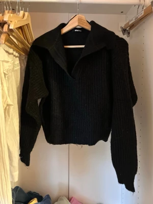 Svart stickad tröja med krage - Säljer en svart stickad tröja från Gina Tricot med bred krage och v-ringad öppning framtill. Tröjan har lång ärm och ribbad struktur som ger en snygg och avslappnad look. Perfekt att matcha med jeans eller kjol.
