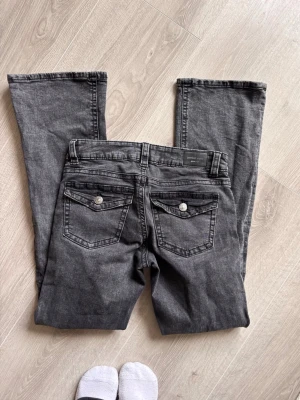 Grå bootcut jeans från Esprit - Säljer ett par grå bootcut jeans från Esprit med snygga bakfickor med lock och silverknappar. Jeansen har klassisk femficksdesign och är tillverkade i mjuk denim med lätt tvättad look. Perfekta för en avslappnad och trendig stil.