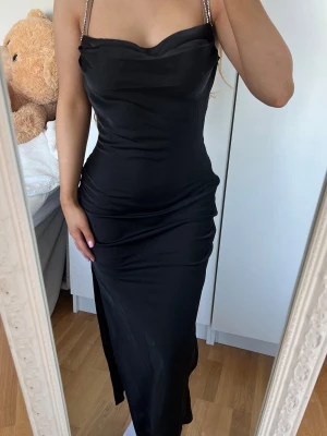 Svart långklänning  - Säljer en elegant svart långklänning med smala, glittriga axelband och draperad urringning. Klänningen har en figurnära passform och en slits på sidan för extra stilpoäng. Perfekt för dig som vill sticka ut på nästa event! Storlek XS/S, ny med prislapp kvar då den tyvärr ej kom till användning 🖤