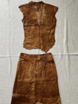 Brun mocka  topp med kjol med snörning - Väldigt bra investering!  Sällsynt vintage skulpturell lädertopp Plein Sud – Cirka Y2K och kjol tillverkad i Frankrike  Ett museumsvärt uttalande från början av 2000-talet brun topp i mocka-look med korta ärmar och cool snörning vid halsen. Asymmetrisk designat kjol med dekorativa nitar och råa kanter ger en edgy cowboy-vibe. Perfekt för dig som vill sticka ut med en statement piece. Viking dress. Nypris är ca 50 000-70 000 kr