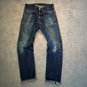 Mörkblå raka jeans med slitningar - Säljer ett par mörkblå selvedge jeans från warehouse med raka ben och tydliga slitningar på framsidan. Jeansen har klassisk femficksdesign, knappgylf och kontrastsömmar. Materialet är kraftig denim i bomull. Perfekta för en avslappnad och trendig look.