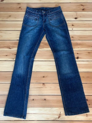 Diesel jeans mörkblåa med låg midja utsvängda bootcut - Säljer ett par klassiska blå bootcut jeans med låg midja och snygga slitningar. Jeansen har fem fickor, dragkedja och knapp framtill samt kontrastsömmar. Perfekta till en avslappnad stil och passar till det mesta i garderoben.