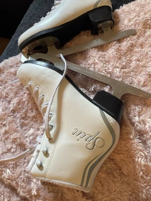 Vita konståkningsskridskor Spin 36 - Snygga vita konståkningsskridskor från Spin med klassisk snörning och silverfärgade detaljer. Skridskorna har robusta stålskenor och svart klack. Perfekta för isbanan och vintersport. Storlek 36 enligt EU-mått.