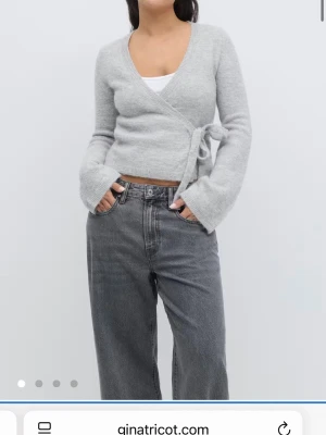 Ljusgrå omlottkofta Gina Tricot - Mysig ljusgrå omlottkofta från Gina Tricot med knytband i midjan och långa ärmar. Koftan har en mjuk, stickad känsla och en feminin v-ringning. Perfekt att styla över ett linne eller t-shirt för en avslappnad look.