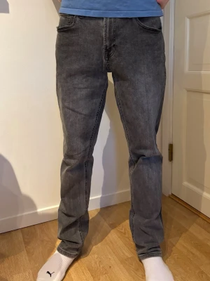 Grå raka jeans i klassisk modell - Säljer ett par grå jeans med rak passform och fem fickor. Jeansen har en klassisk look med normal midja och subtil tvättad finish. Perfekta för dig som gillar en enkel och stilren stil. Materialet är denim i bomull.