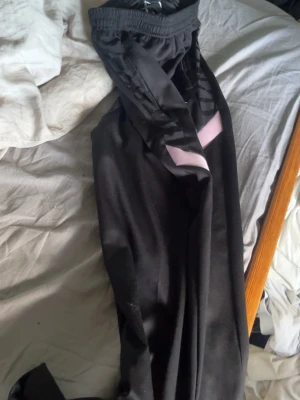 Svarta PSG träningsbyxor Nike - Säljer ett par svarta träningsbyxor från Nike med Paris Saint-Germain-logga och rosa detaljer. Byxorna har resår i midjan och smal passform, perfekta för fotboll eller gym. Materialet är mjukt och stretchigt för maximal komfort.