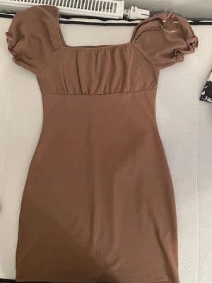 Kort beige klänning med puffärm - Säljer en kort beige klänning med puffärmar och fyrkantig ringning. Klänningen har en figurnära passform och är tillverkad i ett mjukt material som känns bekvämt mot huden. Perfekt för dig som gillar en enkel men trendig stil.