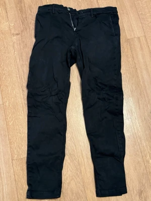 Svarta chinos från Replay - Snygga svarta chinos från Replay. Klassisk modell och smal passform. Byxan har bälteshällor, dragkedjegylf och är tillverkade i ett mjukt denimtyg som ger en bekväm känsla. Perfekta för en stilren och avslappnad look. Storlek - 30x30