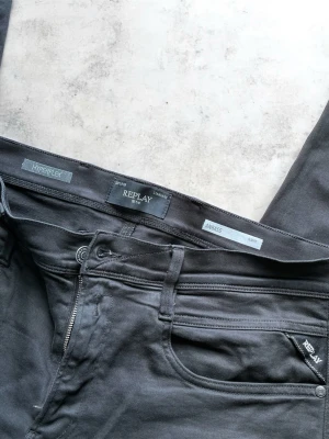 Svarta Replay Hyperflex jeans - Säljer ett par svarta Replay Hyperflex jeans, modell Anbass. Jeansen har smal passform, klassisk femficksdesign och stretchigt material för extra komfort. Perfekta för dig som gillar stilrena och bekväma jeans med modern look.