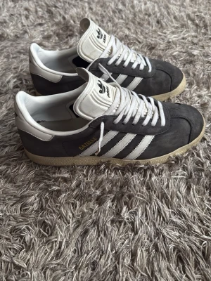 Archive Adidas Gazelle special edition - Säljer ett par klassiska Adidas Gazelle sneakers i grå/blå mocka med vita detaljer och vita. Skorna är lite använda men fortfarande i bra skick. Låg modell med retrovibe, perfekt för dig som gillar stilrena och tidlösa sneakers. Storlek 39. Colorway på denna är limited och svår att hitta.  Hör av er vid funderingar😃