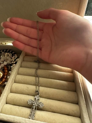 Silverfärgat halsband med korshänge - Snyggt halsband i silverfärg med ett stort korsformat hänge dekorerat med glittrande pärlor. Kedjan är tunn och smidig, och korset har detaljerade kanter som ger en cool och elegant look. Perfekt accessoar för att lyfta din outfit.