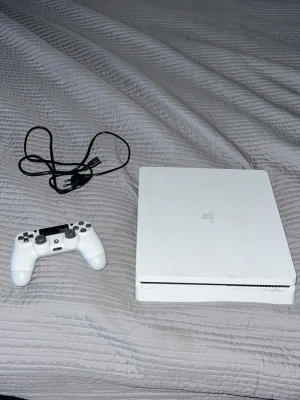 Vit PlayStation 4 Slim med handkontroll - Säljer en vit PlayStation 4 Slim med tillhörande vit DualShock 4-handkontroll och hdmi kabel. Konsolen har en stilren, rektangulär design i plast och passar perfekt för gaming och streaming.