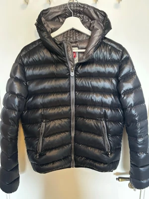 Svart pufferjacka med huva - Snygg svart pufferjacka från colmar med glansig finish och vadderad design. Jackan har två dragkedje fickor, hel dragkedja framtill och en stor huva och riktigt skön att bära. Pris kan diskuteras🙌🏻
