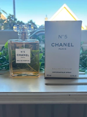 Chanel No 5 Eau de Parfum 100 ml - Chanel No 5 Eau de Parfum i klassisk vit och guldig förpackning. Flaskan rymmer 100 ml och är en ikonisk doft från Chanel, känd för sin eleganta och tidlösa design. Perfekt för dig som vill ha en lyxig parfym med exklusiv känsla.