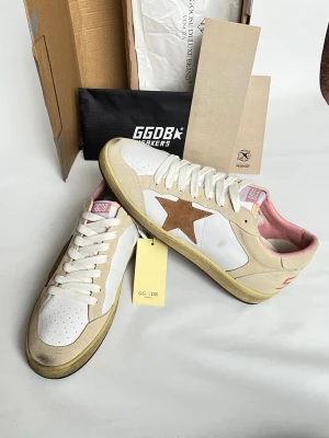 Golden Goose vita och beige sneakers - Golden Goose sneakers i vitt och beige läder med bruna mockadetaljer och den ikoniska stjärnan på sidan. Skorna har vita snören, perforerad tå och rosa innerfoder. Snygg vintagekänsla och klassisk låg modell som passar till många stilar.