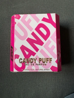 Candy Puff Eau de Parfum 100ml - Candy Puff Eau de Parfum från Omerta kommer i en färgstark rosa och vit förpackning med stora bokstäver. Flaskan innehåller 100 ml och är en naturlig spray. Doften har en söt och ungdomlig känsla, perfekt för dig som gillar lekfulla och fräscha parfymer. Oanvänd 