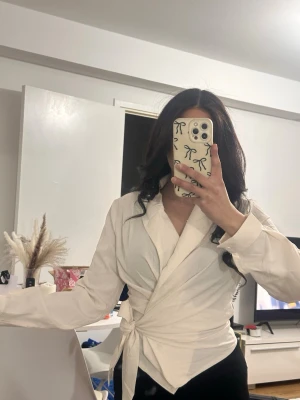 Vit omlottblus med knytband - Stilren vit omlottblus med långa ärmar och knytband i midjan. Storlek S