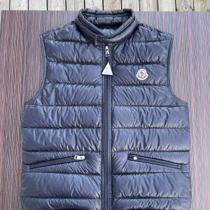 Moncler Gui väst - Moncler Gui Väst (Navy) Size: 1 (XS-S) Skick: 9,5/10 endast ett litet fel då huvudet på dragkedjans vänstra ficka är av! Pris: 3300kr Extra knappar följs med vid köp även Tag! 