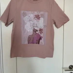 En dovt rosa lätt oversized T-shirt med tryck på en kvinna med blommor. Tröjan är använd men i bra skick. Säljer då den inte riktigt är min stil längre🤍