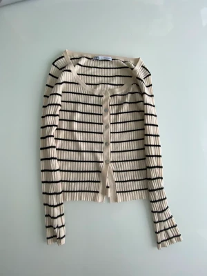 ZARA Beige randig kofta - En lätt, enkel och vacker kofta.  Den kommer i färgen beige tillsammans med tunna svarta ränder.  Tyget känns mjukt och skönt och tröjan känns bekväm att ha på sig. Har används en gång.  Köparen står för frakten.