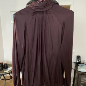 Plommonfärgad blus från Soyaconcept - Denna blus med hög krage har ett fantastiskt fall. Den har knappar i nacken och en liten mudd längs ned. Den är sparsamt använd så finns inget att anmärka på.