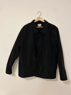 Svart overshirt - Georg Overshirt från Weekday i blankt material. Superfin men endast använd ett par gånger pga för liten i storleken. Finns i Stockholm men kan skickas.  Nypris ca 500kr.  