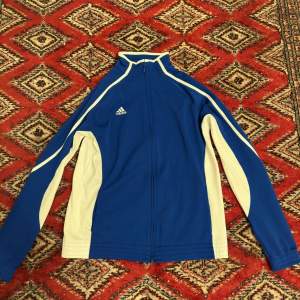 En vintage Adidas tracksuit från 90-talet, blå vit men ser lite gul ut pågrund utav av lampan jag har. Storleken är M men sitter som S