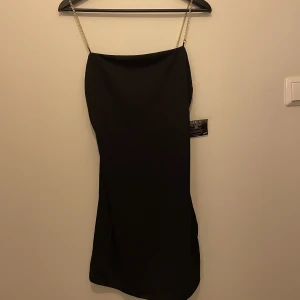 Klänning - Klänning med axelband i guldiga kedjor. Köpt från Nelly, aldrig använd o lappen sitter kvar. Sitter lite lösare men ändå väldigt smickrande på!