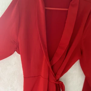 Blus - En röd blus som knyts runt kroppen. Satin inspirerat tyg. Passar en strl S-M