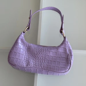 Lila väska  - Fin väska från Nelly i en ljuslila färg med guldiga detaljer, helt oanvänd 💜