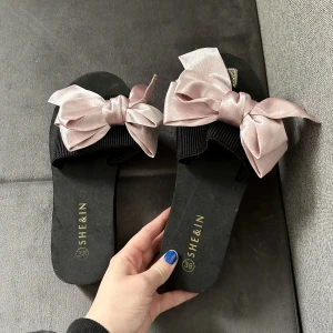 Tofflor  - Säljer nu ett par svarta tofflor med rosa rosett, de är från SHEIN men är aldrig använda endast testade säljer på grund av att dom aldrig kommer till användning 