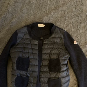 Moncler Cardigan - Säljer min jättefina marinblåa cardigan från moncler, har en liten defekt men inget märkvärdigt. Har inte äktehetsbevis men den är köpt på vestaire där de endast säljs äkta kläder. Storlek M men passar mig som vanligtvis har S