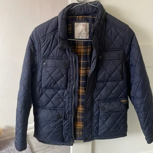 Quiltad Jacka - Snygg praktisk Junior Jacka i marinblått, passar perfekt till vår som höst, knappt använd, i st 9-11 år! Jackan har en inbyggd tunn luva innanför kedjan vid kragen! Den är som ny, har även en till i större storlek i militärgrönt! 