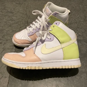 Nike Dunk High 37,5 - Har små små tecken på slitage men är överlag mycket fräscha (använda vid två tillfällen).  Swoshen är ljusgul.  Skon är i övrigt vit med pasteller i limegul, ljuslila och rosa, stlk 37,5. Nypris 1249kr —men är slutsålda.