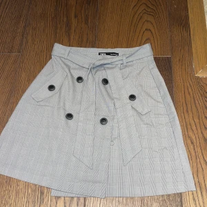 Kjol från Zara - Grå rutig kjol med knappar från Zara, man kan ta bort bältet som sitter i midjan om man vill. Storlek M, 70kr+frakt