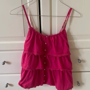 rosa volanglinne - Superfint och somrigt linne med knappar från hollister. Banden är justerbara och linnet går i stora fina volanger. Passar helt perfekt till sommaren! Bara att höra av er om ni undrar något🥰