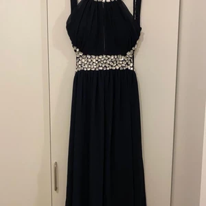 Festklänning   - Klänning med vackra stenar runt midja hals och axelband .Tunnt band knyts bak hals, bar rygg, fodrad, polyester Färg : mörkblå Storl: 12 (38/40) Hämtas Brandbergen alternativ skickas med post mot avgift