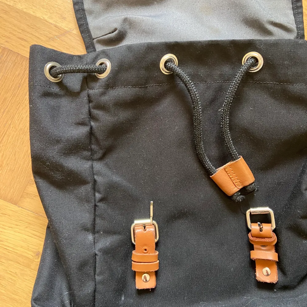 En rymlig svart ryggsäck med bruna ödet detaljer, använd under flera års tid. Den är helt och ren förutom att den ena spännet har lossnat på framsidan. Men den fungerar ändå för du sluter igen väskan med bandet. Väskor.