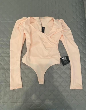Body med puffärmar  - En helt ny body med puffärmar i storlek S. Det står att den är i färgen rosa men i verkligheten är det mer ljus peach. Säljs för 120 (ordinarie pris 349kr). Andra bilden är tagen från Nelly där bodyn köptes. 