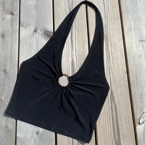 Halter neck topp med guldring  - En topp som skriker ”festens pingla”! Cool guldringsdetalj som sätter pricken över i:et tillsammans med den djupa ryggen. Mycket stretch i materialet. Bara använt 1 gång. NYPRIS: 179kr