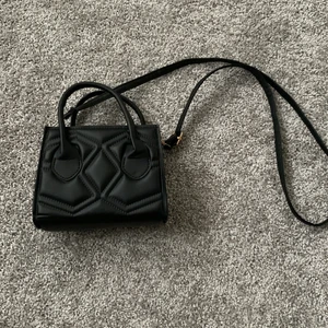 Svart väska  - En svart väska med handtag på bägge sidor och ett långt band som går att reglera. Aldrig andvänd