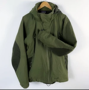 Patagonia jacka L vintage  - Vintage grön jacka från Patagonia.   Troligen från omkring 00-talet med tanke på loggans utseende. Avtagbar huva. Ofodrad.  Fint vintage-skick!  Sökord: Skidjacka, Snowboardjacka, y2k, retro, Snölås.