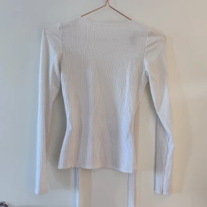 Långärmad topp - Topp med knytning i ryggen. Säljes då den inte kommer till användning. Tyvärr liten fläck på högerärmen, jag har inte fått bort fläcken, men den syns inte när man har den på sig!. Hör av dig om du har frågor!