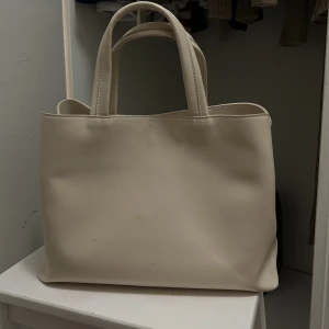 Nakd väska - Säljer denna väldigt stilrena väska från NA-KD. Många fack och tillkommer ett längre axelband. Använd ett fåtal gånger men några småsmå märken framtill, syns knappt. ✨