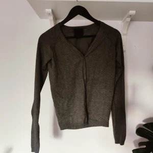 Kofta med glittrande knappar - Tightare, finstickad kofta i mellangrått med små fuskkristaller som knappar. Är en XS men passar även S.